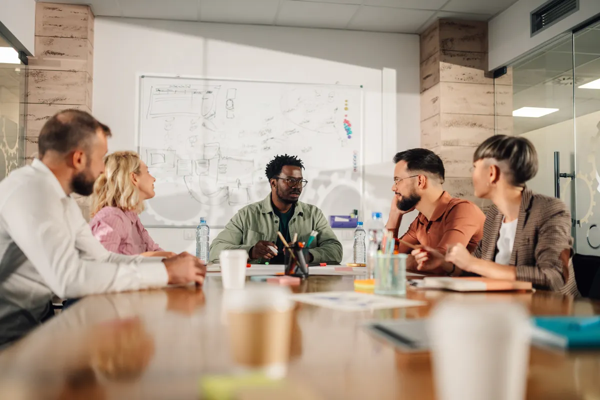 A marketing team in a meeting around a table, with a whiteboard behind them.