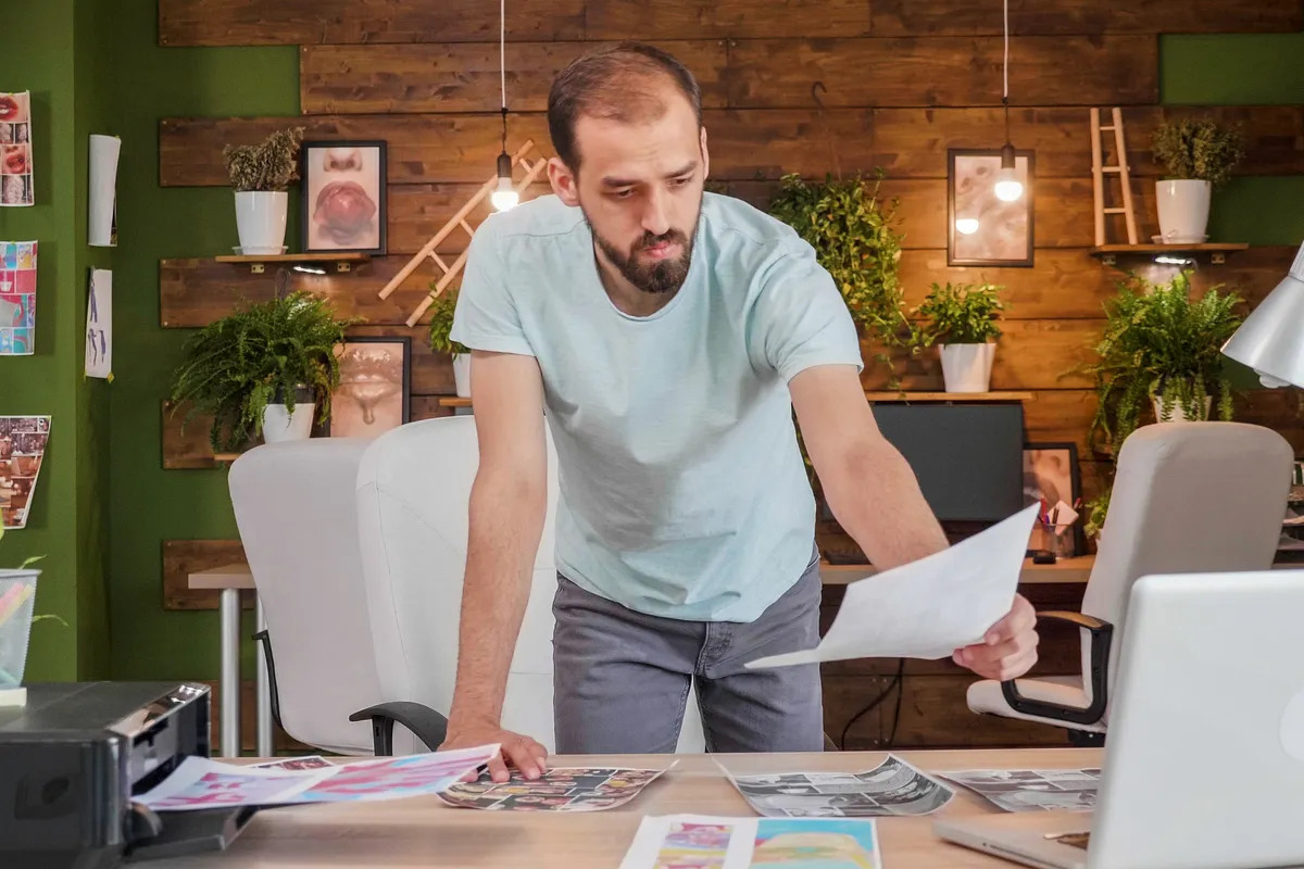 A freelance designer at a studio desk reviewing printed designs.
